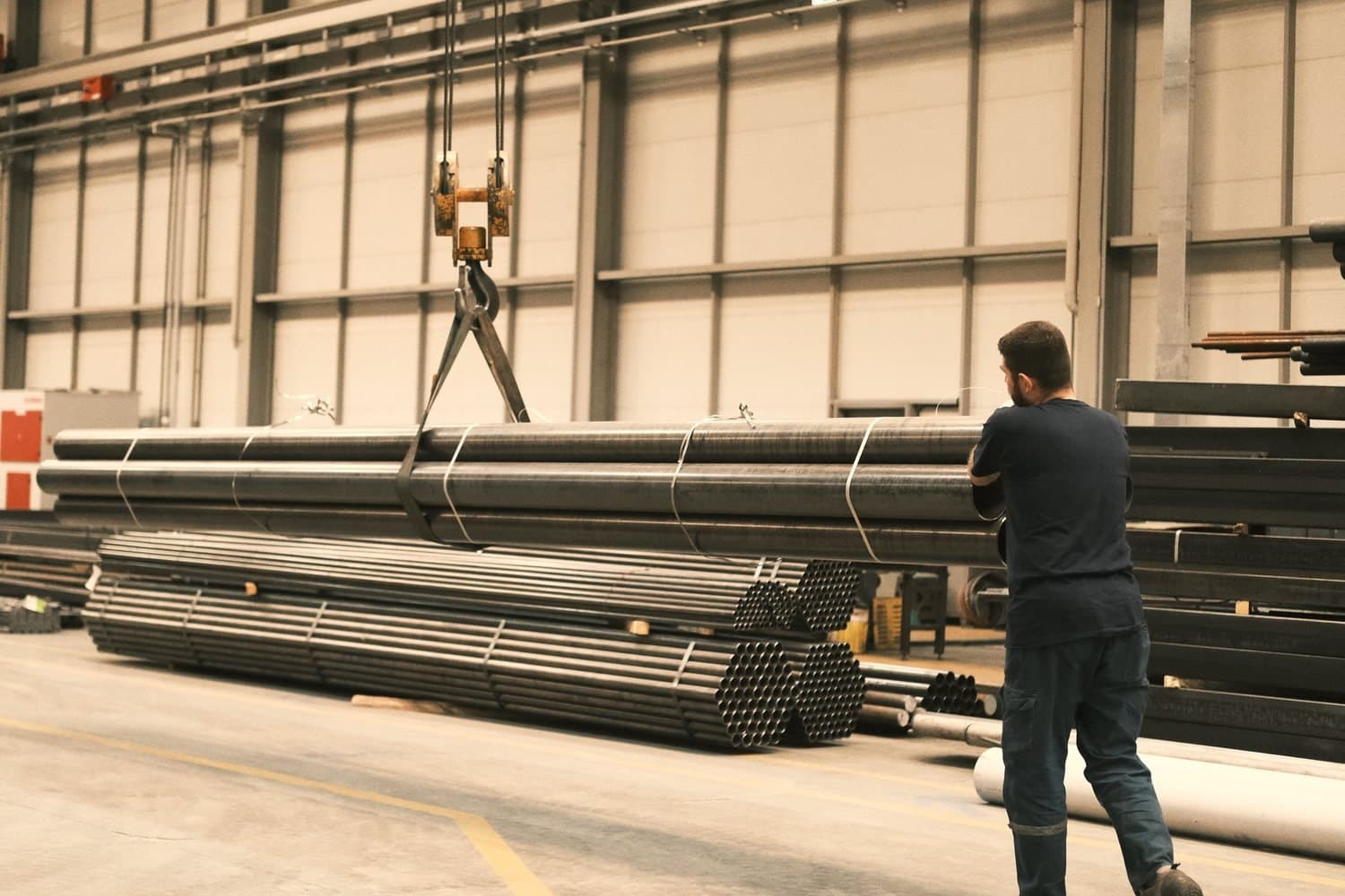 Bundles of steel tube being moved by crane in a clean stockholding hall